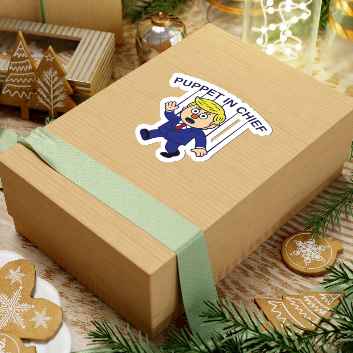 Political Humor Sticker - Puppet in Chief on gift box with festive decor and holiday-themed cookies surrounding it